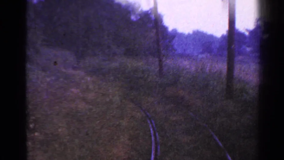 1953 Connecticut 8mm view of railroad tracks curving through a wooded rural area, with dark gate edges and purple color shift.