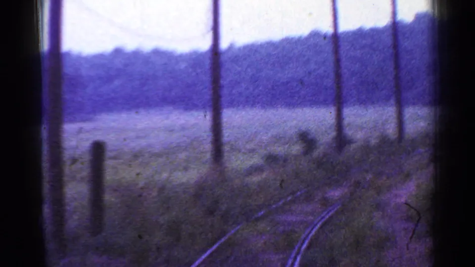 From a moving train in Connecticut, rural tracks bend past poles, brush, fields, and hazy wooded hills.