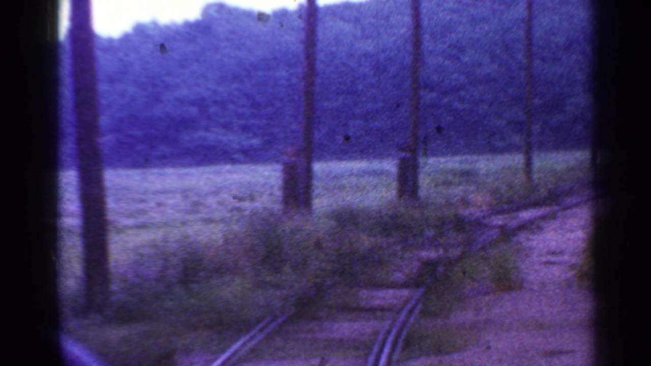 1953 Connecticut 8mm frame showing a dark forward train view along a curving rail line bordered by poles, brush, and trees.