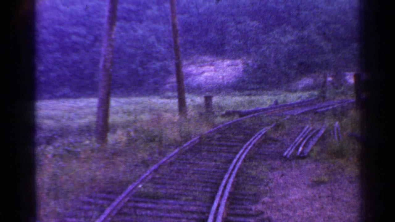 Vintage Connecticut train-view frame with a right-curving track, utility poles, rough vegetation, and a dark wooded backdrop.