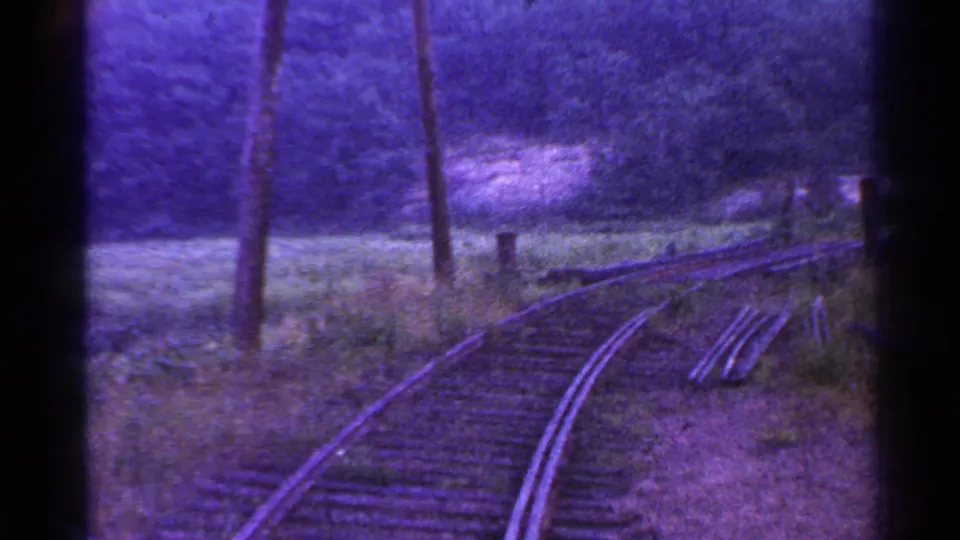 Vintage Connecticut train-view frame with a right-curving track, utility poles, rough vegetation, and a dark wooded backdrop.