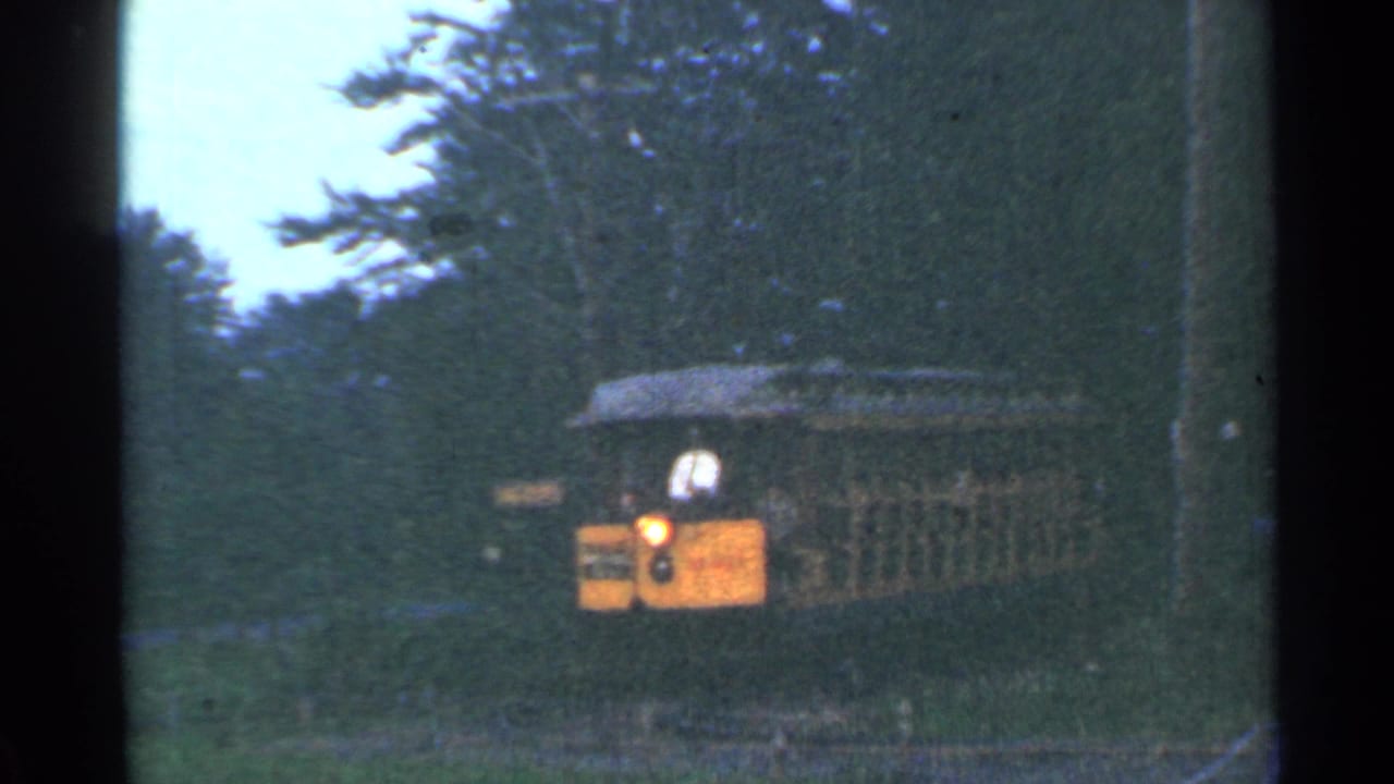 1953 Connecticut 8mm frame of a yellow tram moving through a wooded area, with a driver visible at the front and passengers behind.