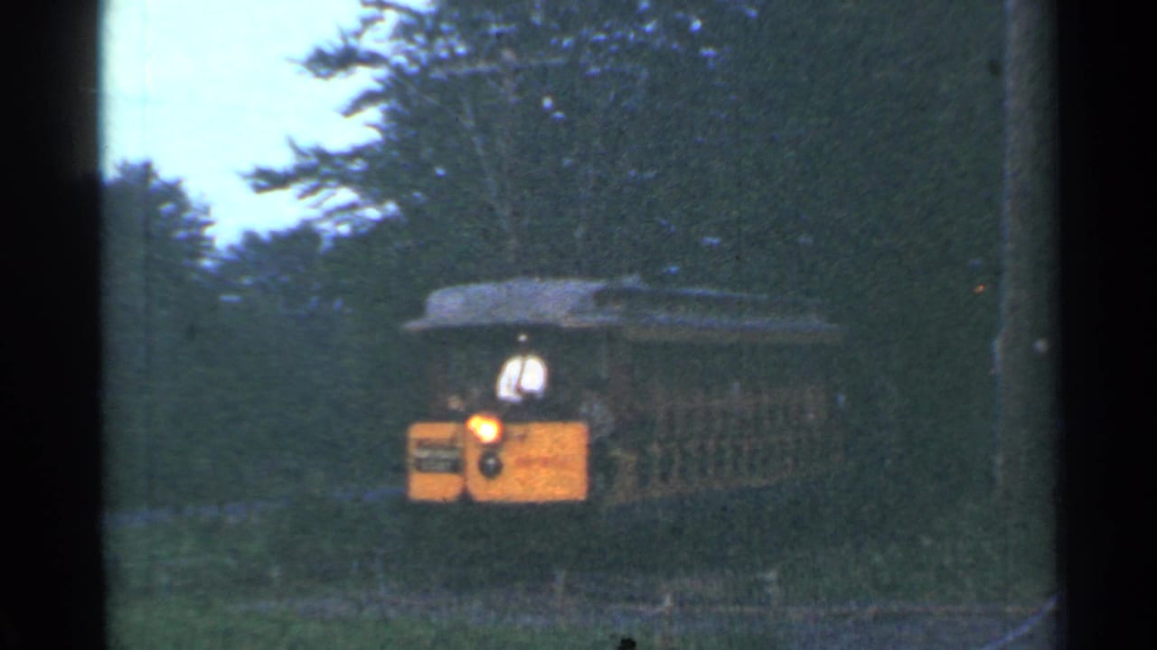 The yellow tram continues toward the camera in the Connecticut woods, with a light-shirted driver and passenger compartment visible.