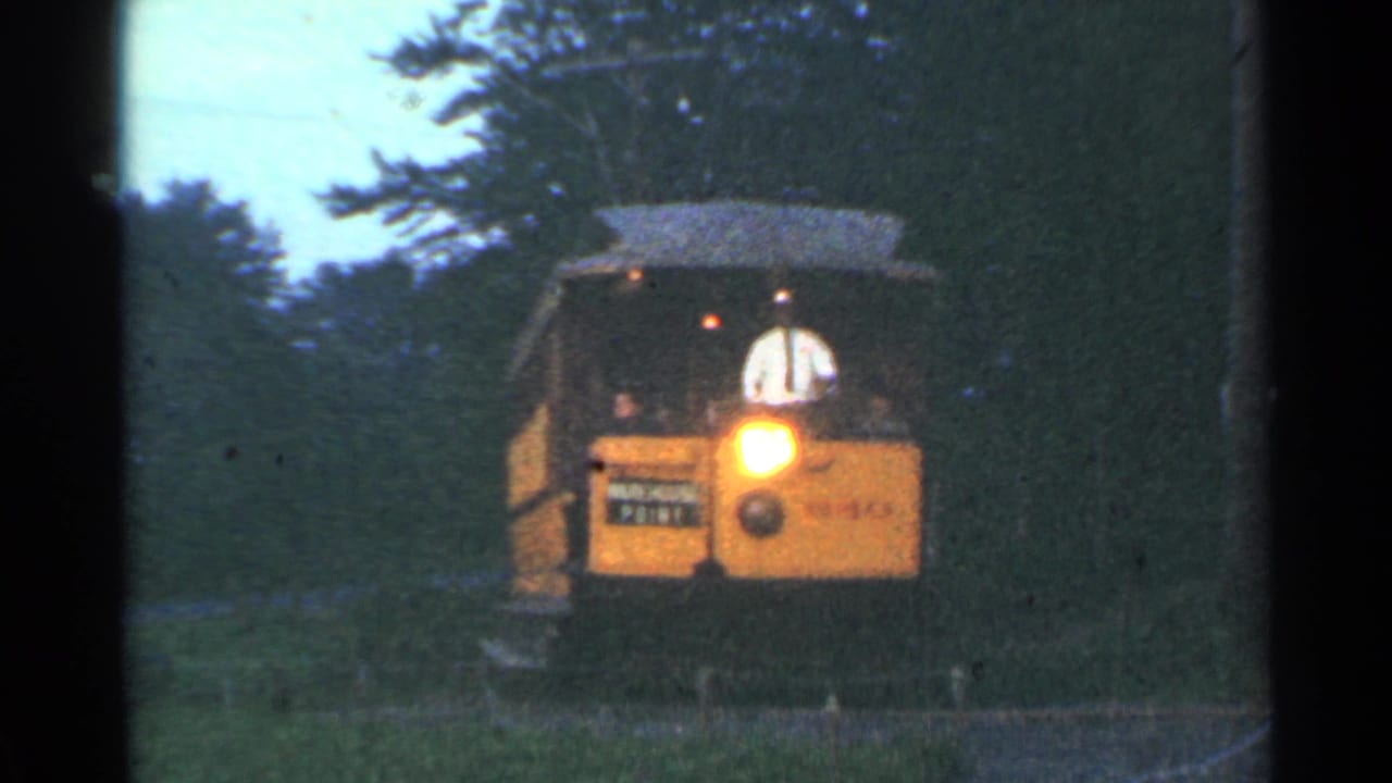 Yellow trolley approaching on wooded track with bright headlight and dark film edge.