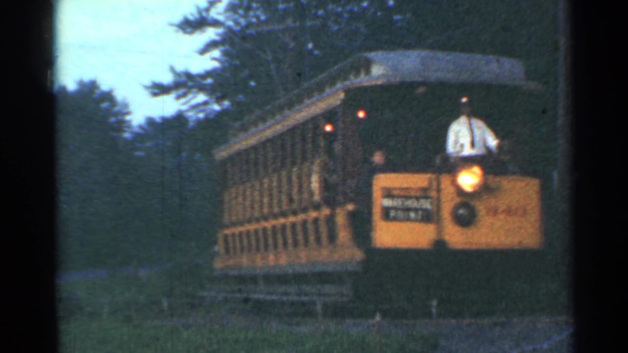Open-sided yellow trolley passing through trees with passengers visible.