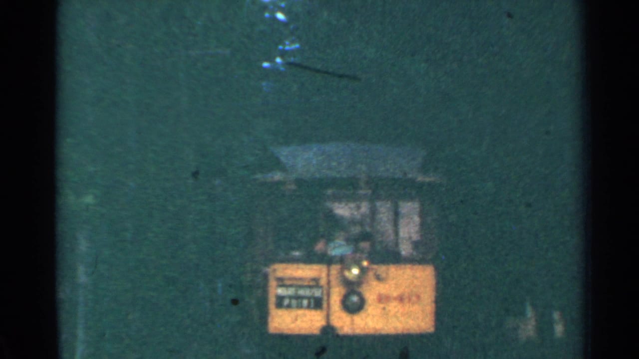 Yellow trolley farther inside a dark green tunnel, seen through heavy grain.