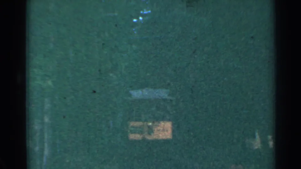 Connecticut 1953 home-movie frame with dark edges, green surroundings, and a faint yellow trolley-like form in the distance.