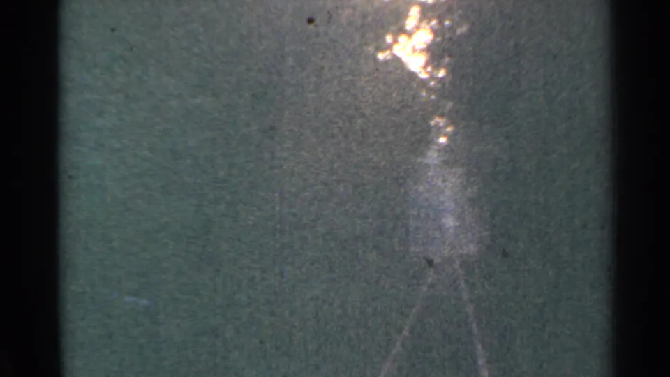 A low-exposure 1953 Connecticut train frame shows a bright flare, heavy grain, and a faint silhouetted figure or reflection.