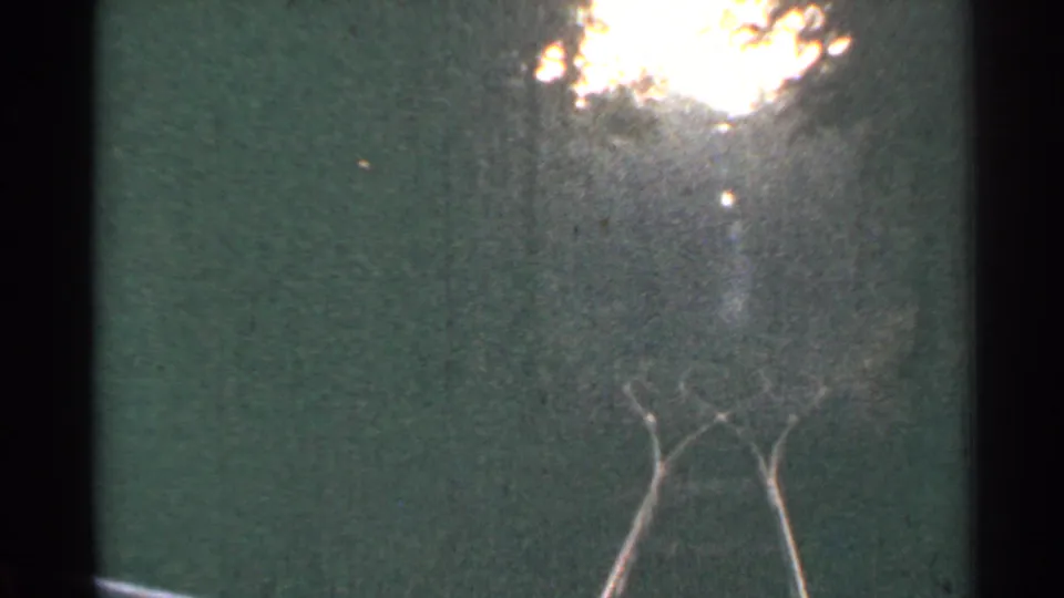 Grainy 1953 Connecticut home-movie frame showing railroad tracks from near ground level, with flare and dust across the scan.