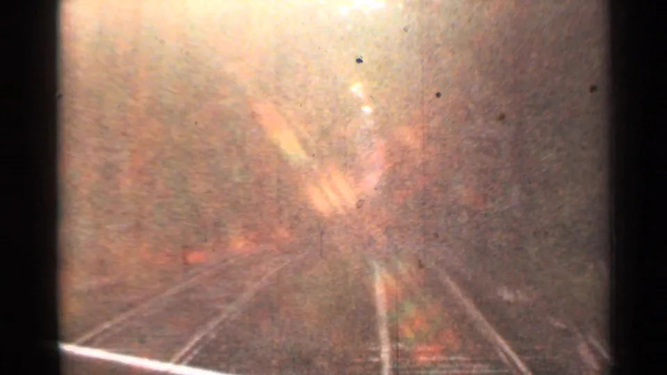 Overexposed 1953 Connecticut 8mm frame looking along tracks in a wooded rail corridor from a moving passenger perspective.