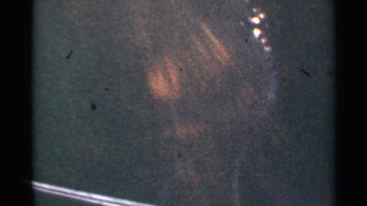 1953 Connecticut 8mm frame showing an indistinct dark green surface, visible film grain, scratches, gate edges, and a faint bright flare.