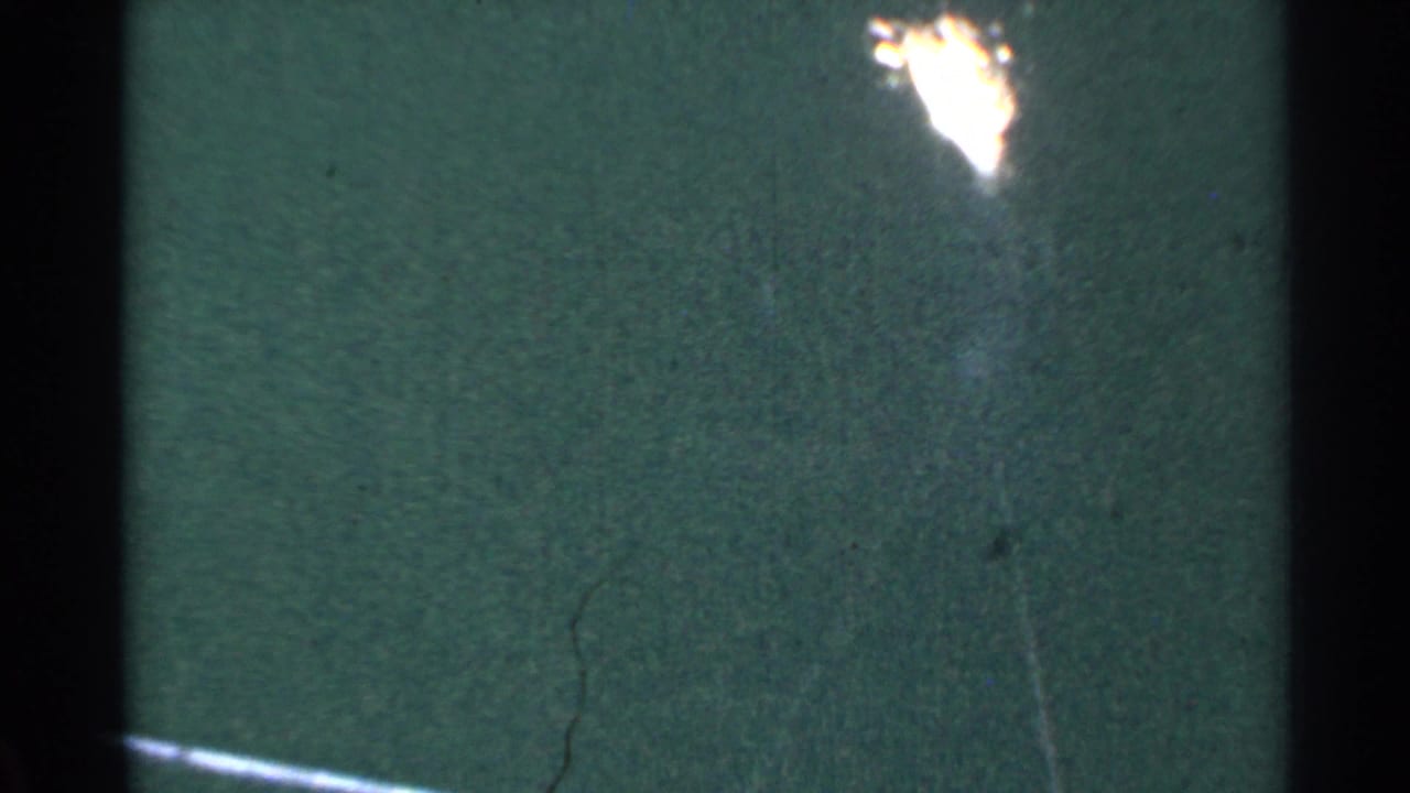 1953 Connecticut 8mm frame with a bright flare over a dark green surface, bordered by black film edges and visible scratches.