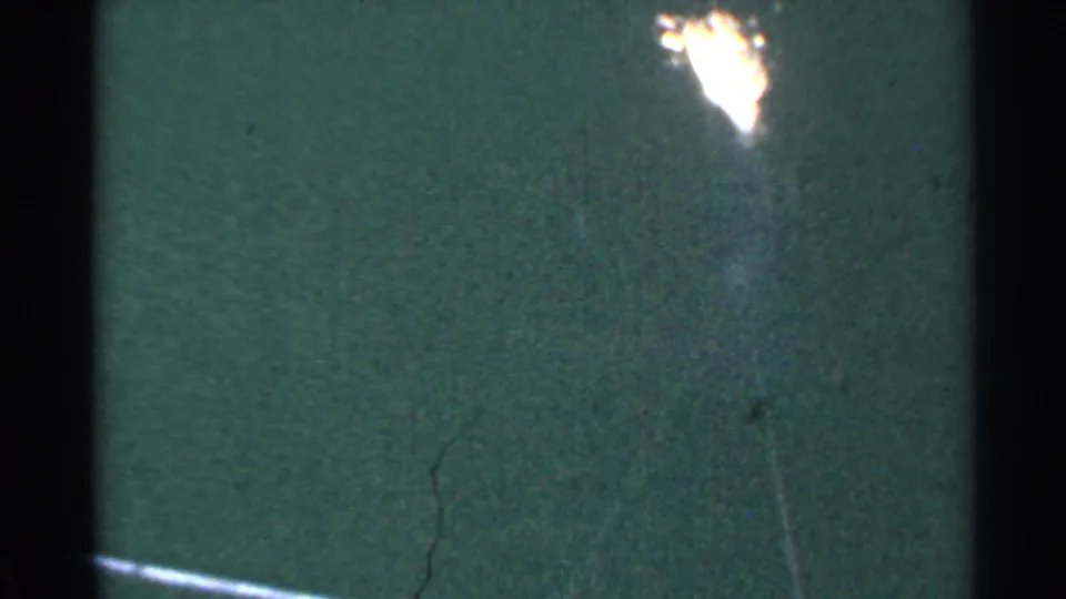 1953 Connecticut 8mm frame with a bright flare over a dark green surface, bordered by black film edges and visible scratches.