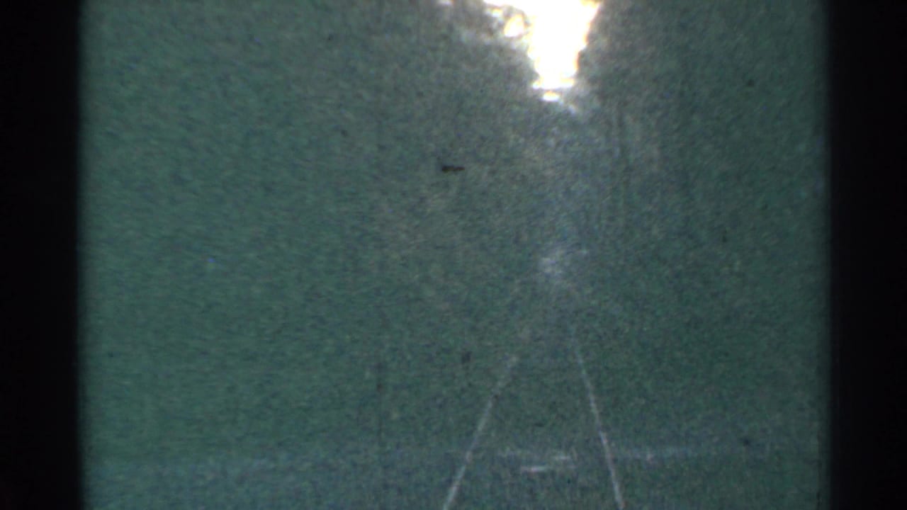 A 1953 Connecticut 8mm frame appears to show faint old rail-like tracks receding into a wooded area under a bright overexposed opening.