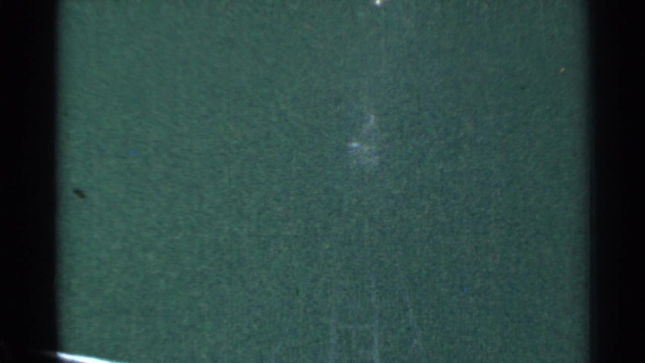 This 1953 Connecticut home-movie frame is mostly dark green film density with faint track detail, scratches, dust, and a shadowed edge from the scanned film frame.
