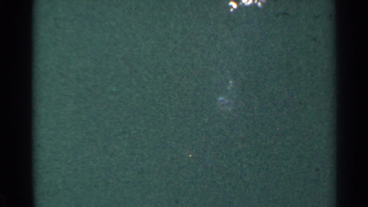The final visible frame is a dim green 8mm view with faint wooded or trackside detail, small bright marks, film grain, and heavy softness.