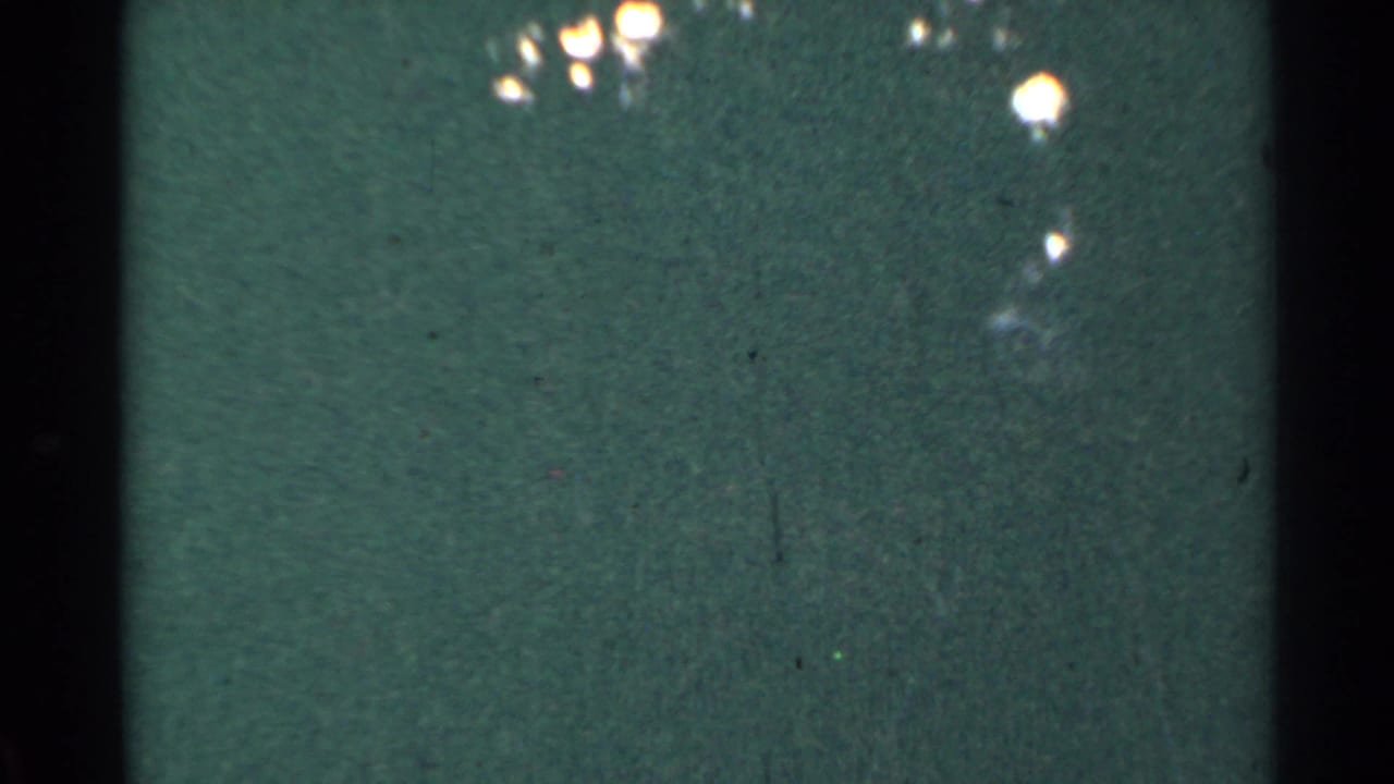 Dim green frame with a central black divider, scratches, grain, and bright highlights near the top.