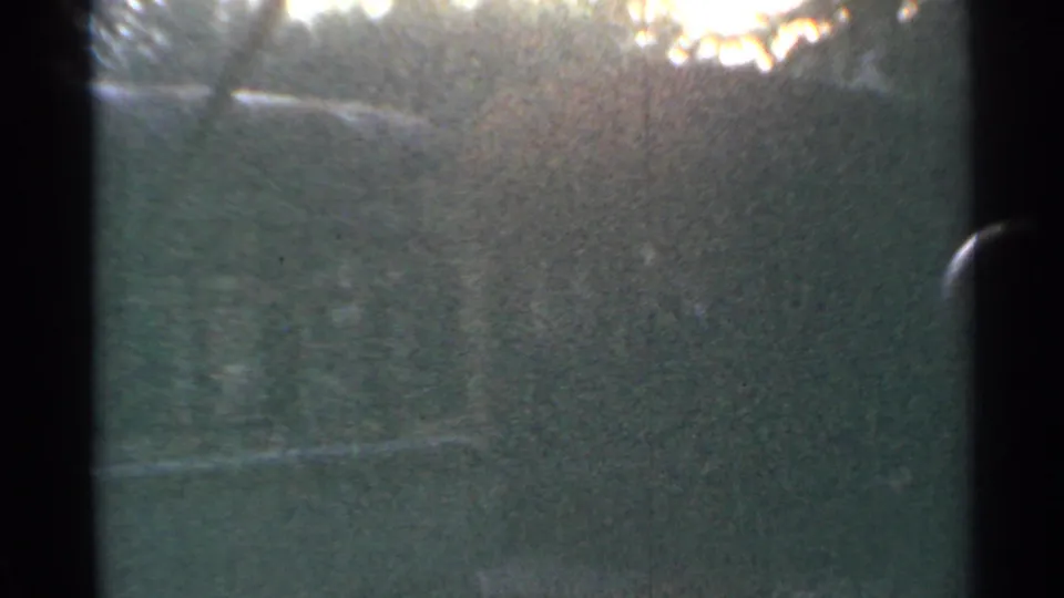 1953 Connecticut 8mm train-window view with dark framing, soft greenery, glare, and visible film grain.