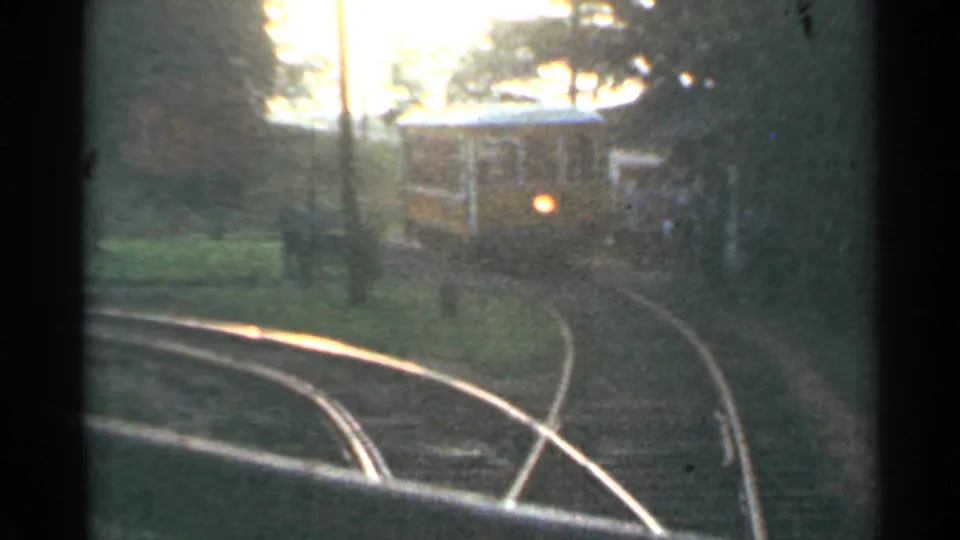 1953 Connecticut 8mm train POV showing curved rails and a yellow railcar ahead in soft evening-like light.