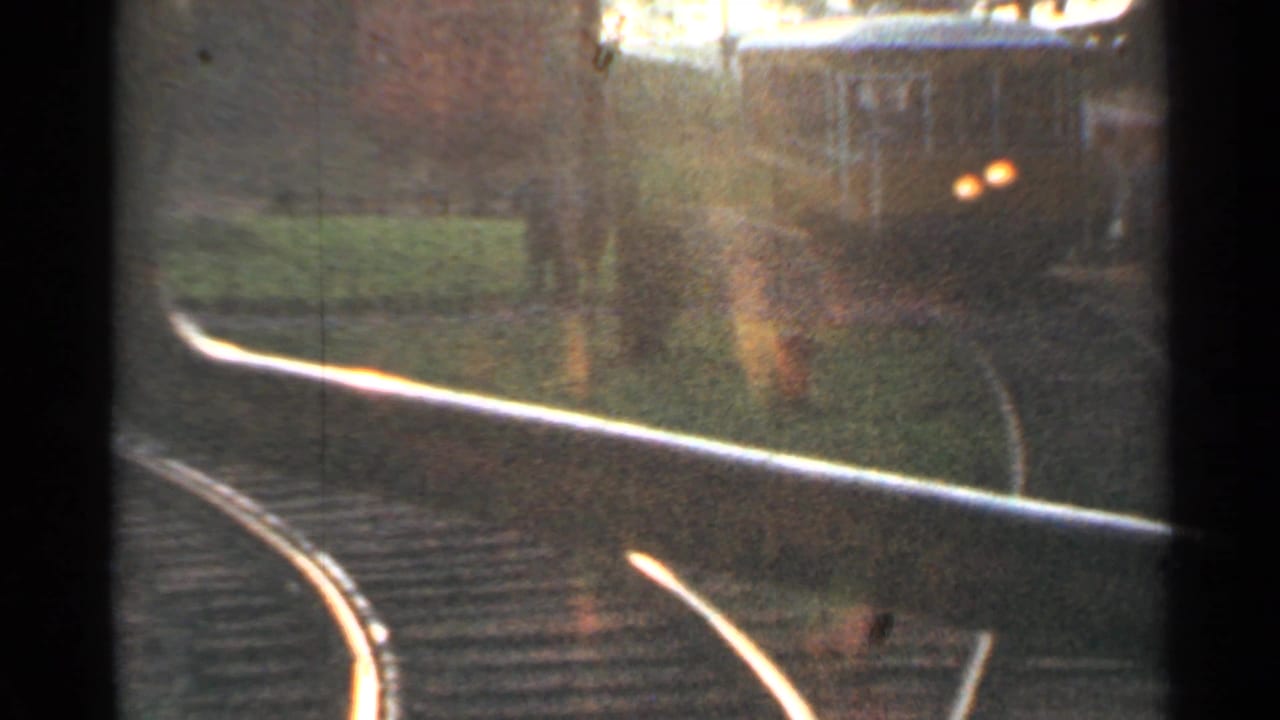 Curved railroad tracks seen from a moving train with a blurred car or station area beyond.