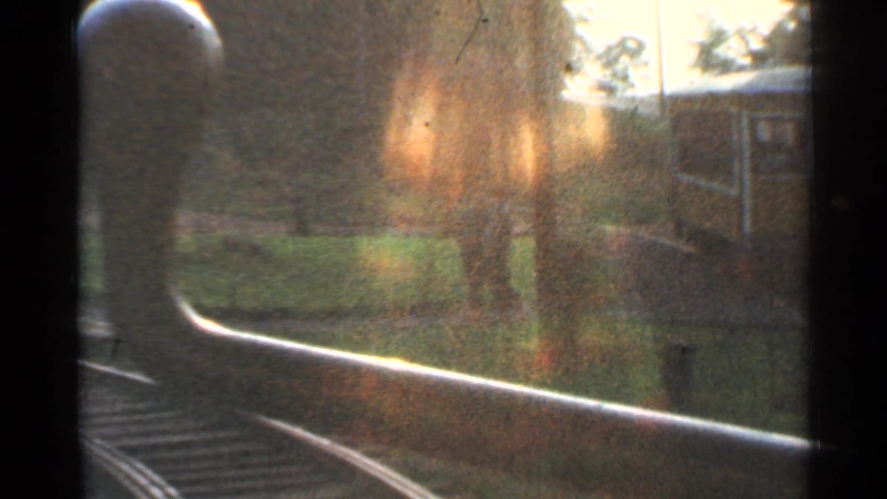 Blurred view along curved rails with a rounded train front and trees beside the track.