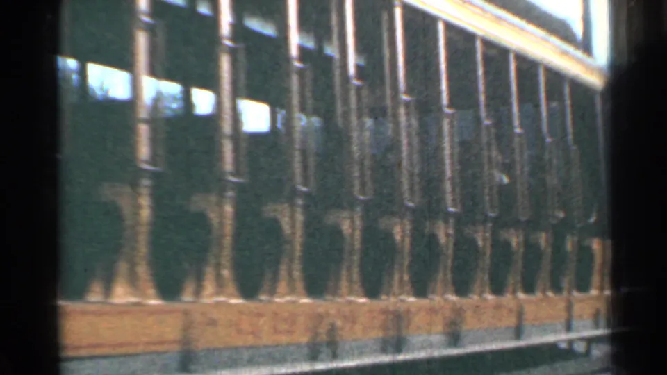 Side view of the yellow trolley in Connecticut, with repeated railings, windows, passenger silhouettes, and trees beyond the car.