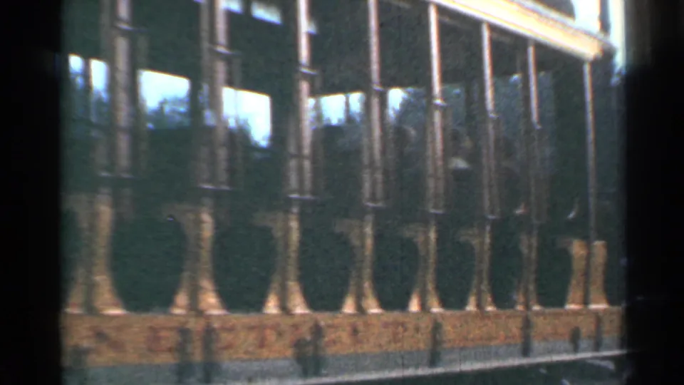 1953 Connecticut 8mm frame of a trolley side moving past shrubs, a low wall, and trackside fencing or curb detail.