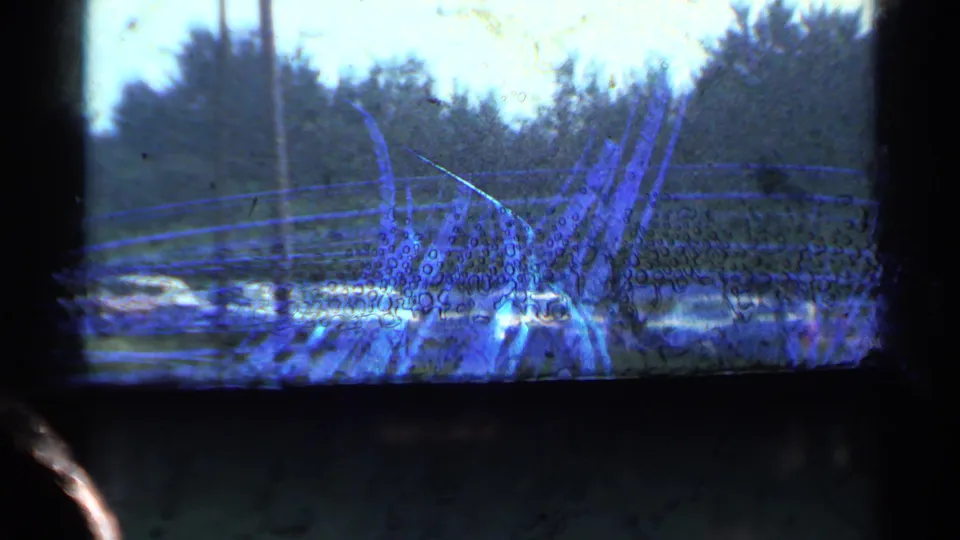 1953 Connecticut 8mm frame showing a curved track or rail structure in the foreground, with cars, trees, and roadside space behind it.