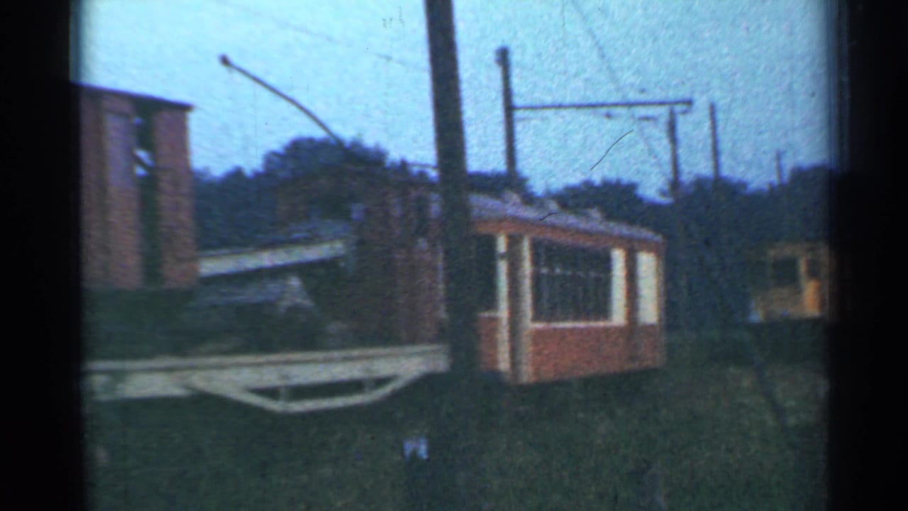 1953 Connecticut 8mm frame showing a red-and-cream rail car near a brick building, with overhead rail lines and utility poles.