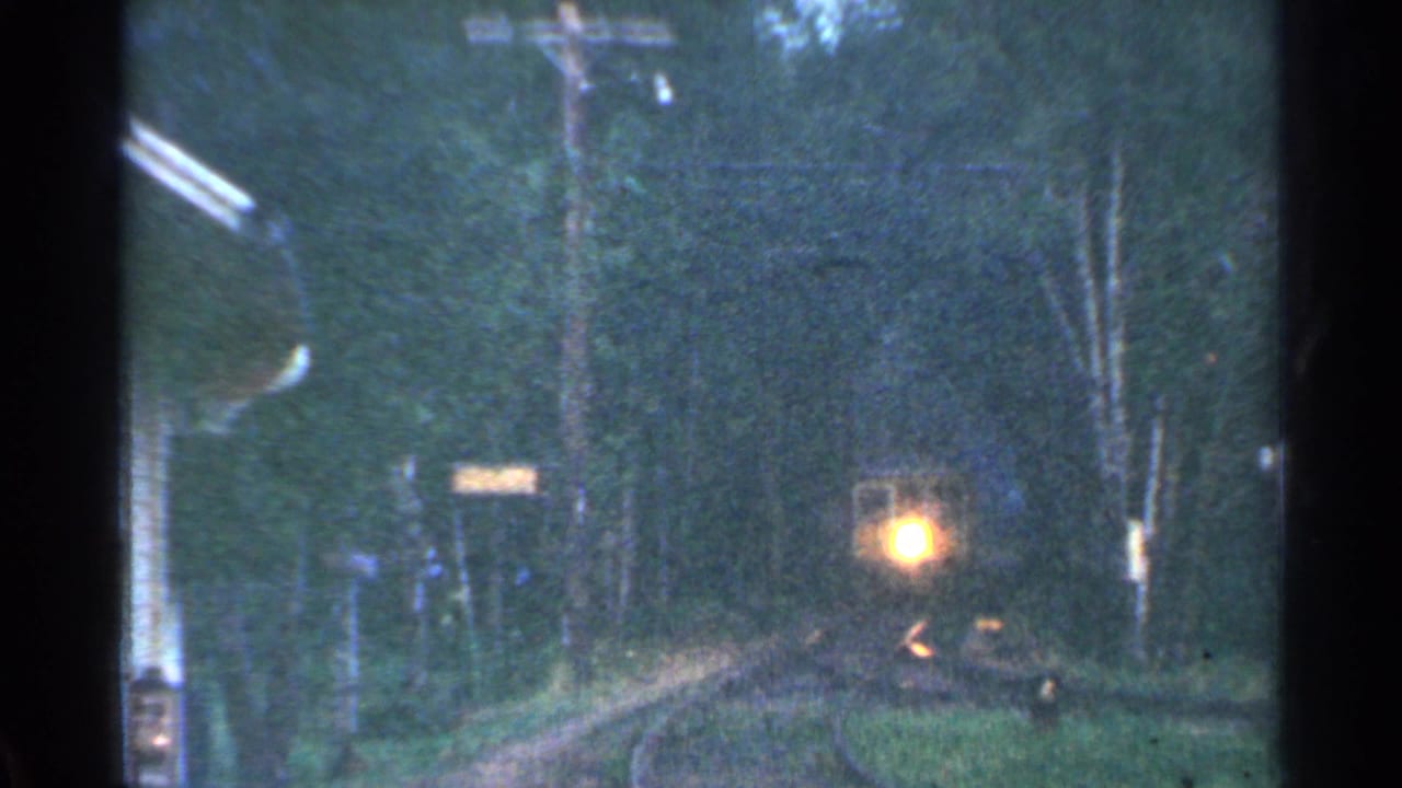 Distant train headlight approaching through a wooded Connecticut trackside view in 1953 home-movie footage.