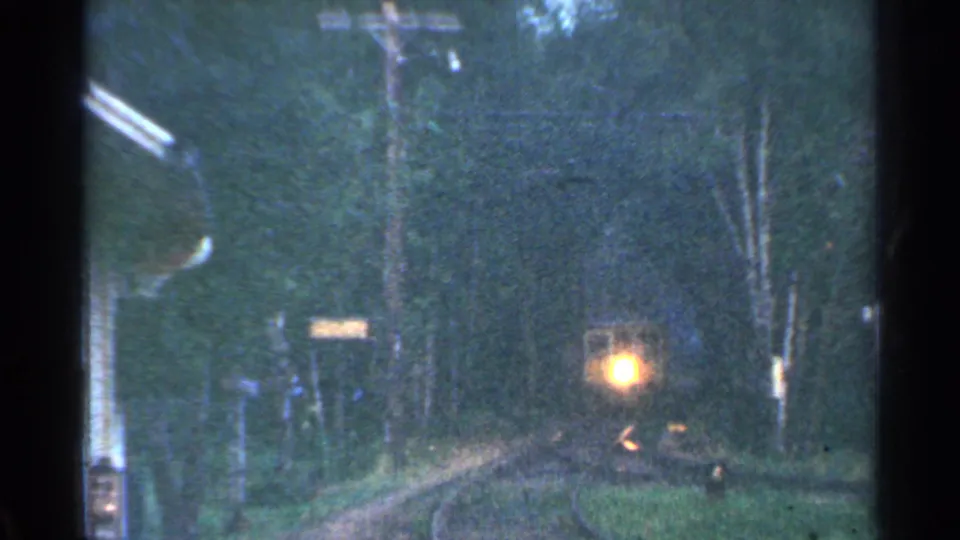 Distant train headlight approaching through a wooded Connecticut trackside view in 1953 home-movie footage.