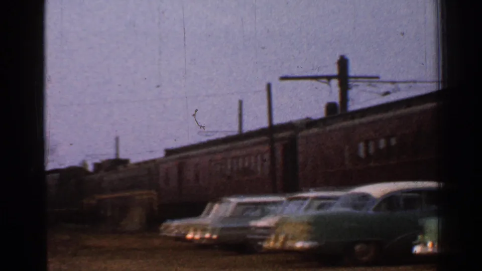 A brown passenger train fills the background behind parked 1950s automobiles in Connecticut home-movie footage.