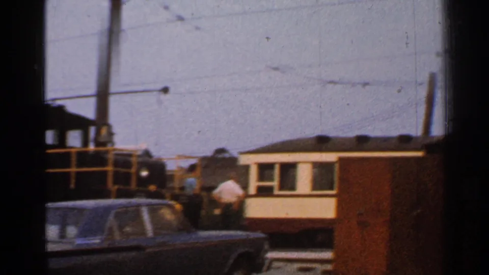 Connecticut 1953 home-movie frame with a dark car, rail cars, and a person standing near train-yard equipment.
