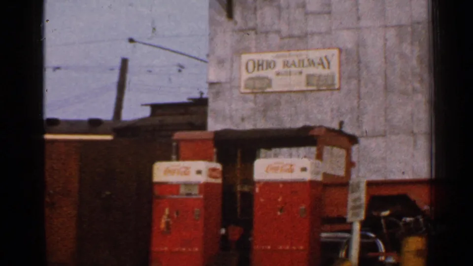 1953 Connecticut frame showing an Ohio Railway sign, red Coca-Cola machines, and rail-yard structures in soft 8mm color.