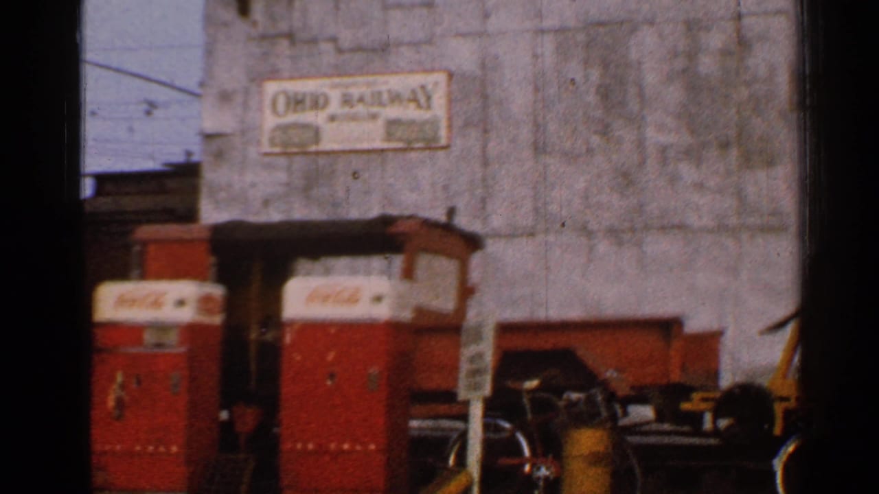 1953 Connecticut 8mm frame showing red Coca-Cola vending machines, a bicycle, and an Ohio Railway sign on a weathered industrial wall.