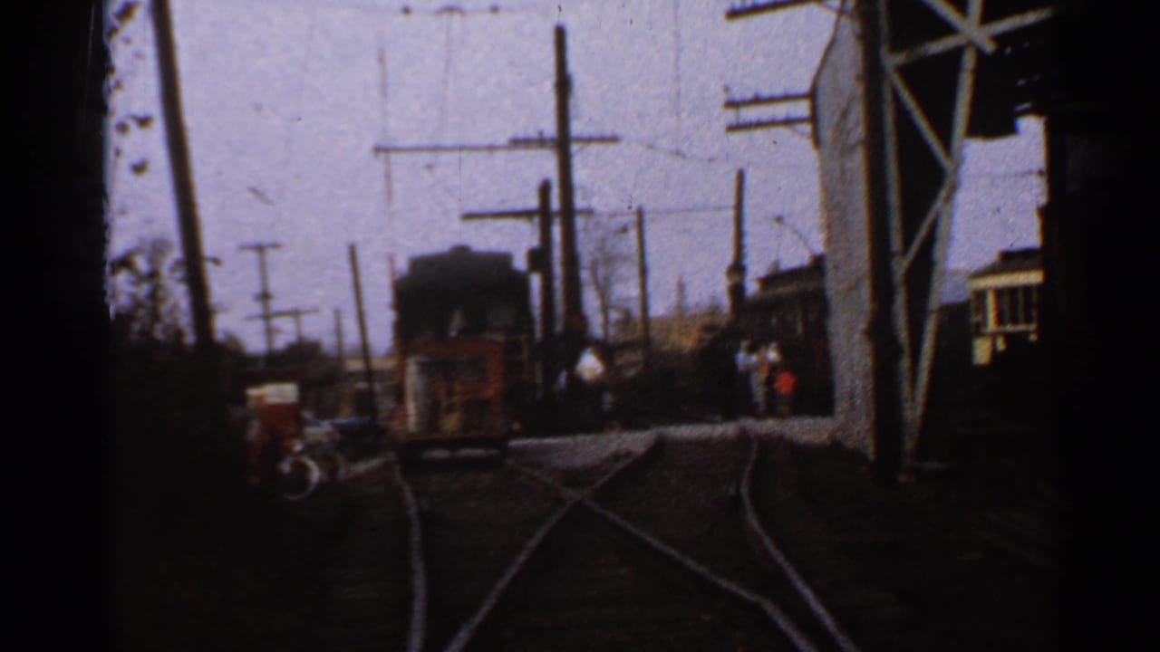 1953 Connecticut rail yard view with curving tracks, overhead electrical wires, utility poles, trolley cars, and a few distant people.