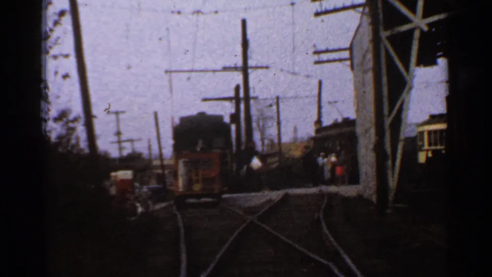 1953 Connecticut 8mm view across multiple rail tracks toward trolley cars, overhead wiring, utility poles, and people near the right side.
