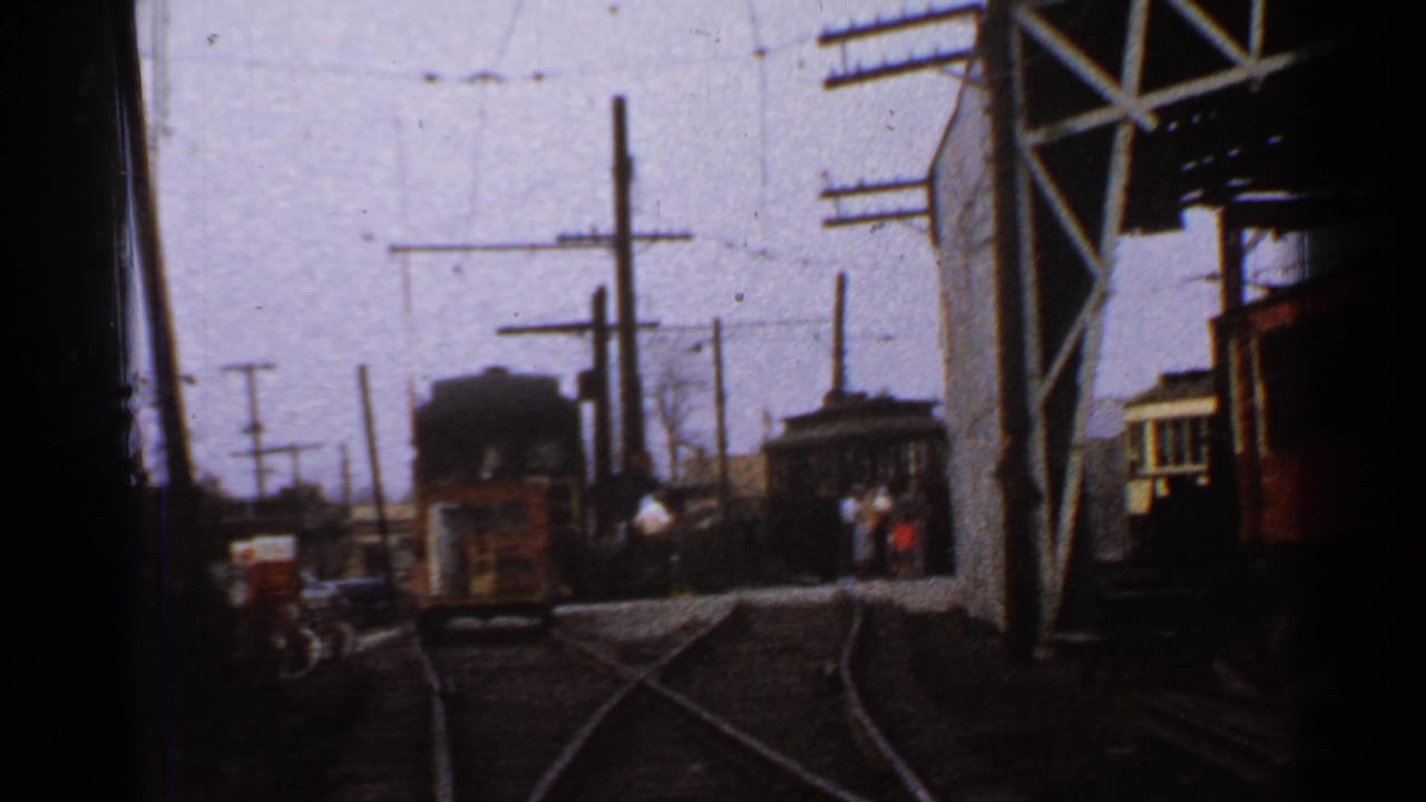 1953 Connecticut 8mm frame showing rail tracks, overhead wires, utility poles, a steel gantry, and railcars in a yard setting.
