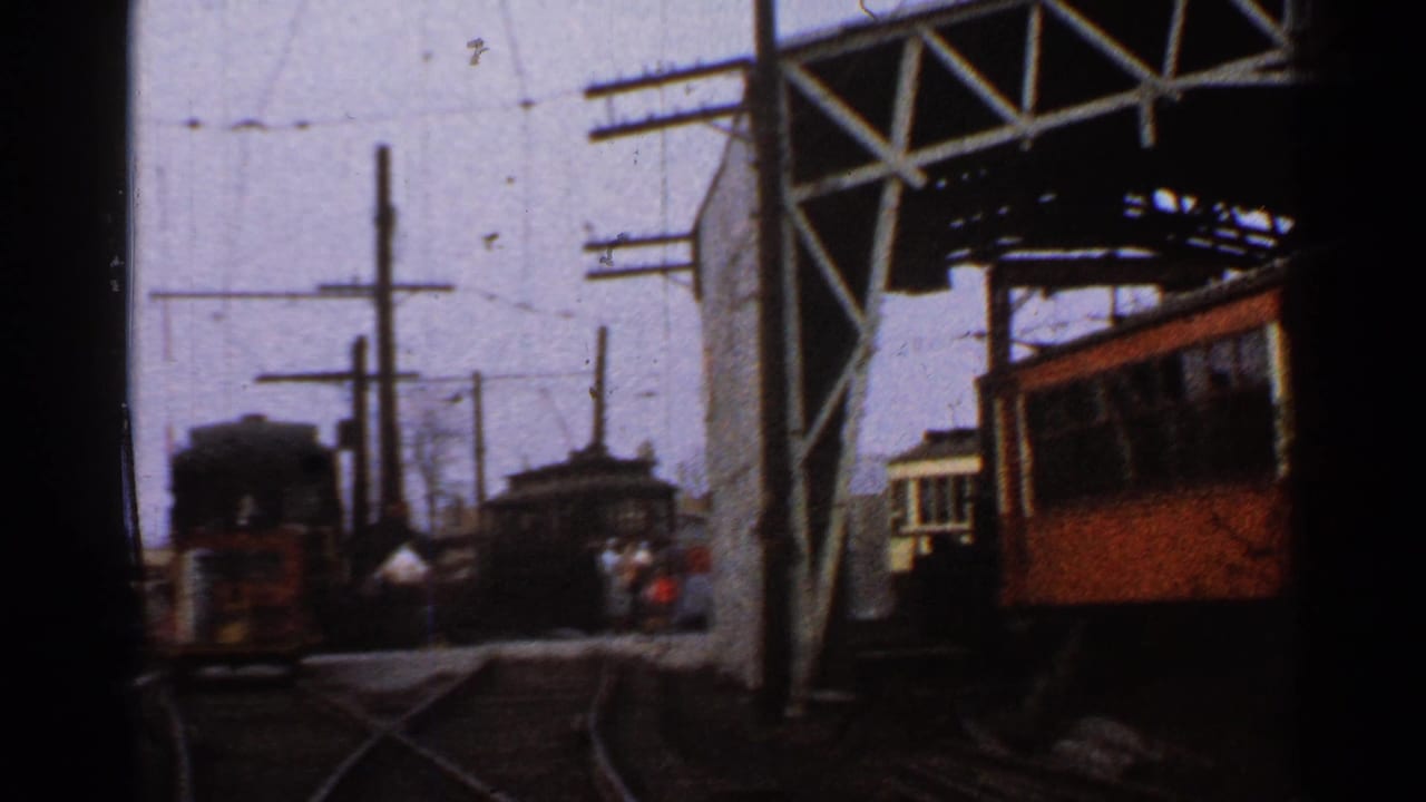 1953 Connecticut rail-yard view with an orange railcar at right, darker rail equipment ahead, overhead wires, and a large metal gantry.