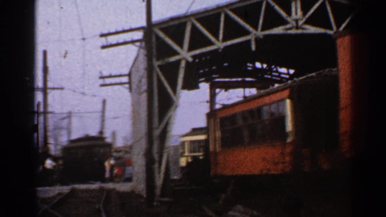 Connecticut 1953 home-movie frame showing multiple railcars, intersecting tracks, utility poles, overhead wires, and small people near the rail yard.