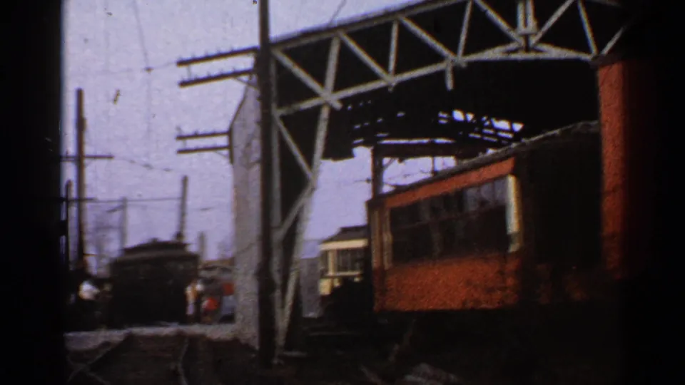 Connecticut 1953 home-movie frame showing multiple railcars, intersecting tracks, utility poles, overhead wires, and small people near the rail yard.