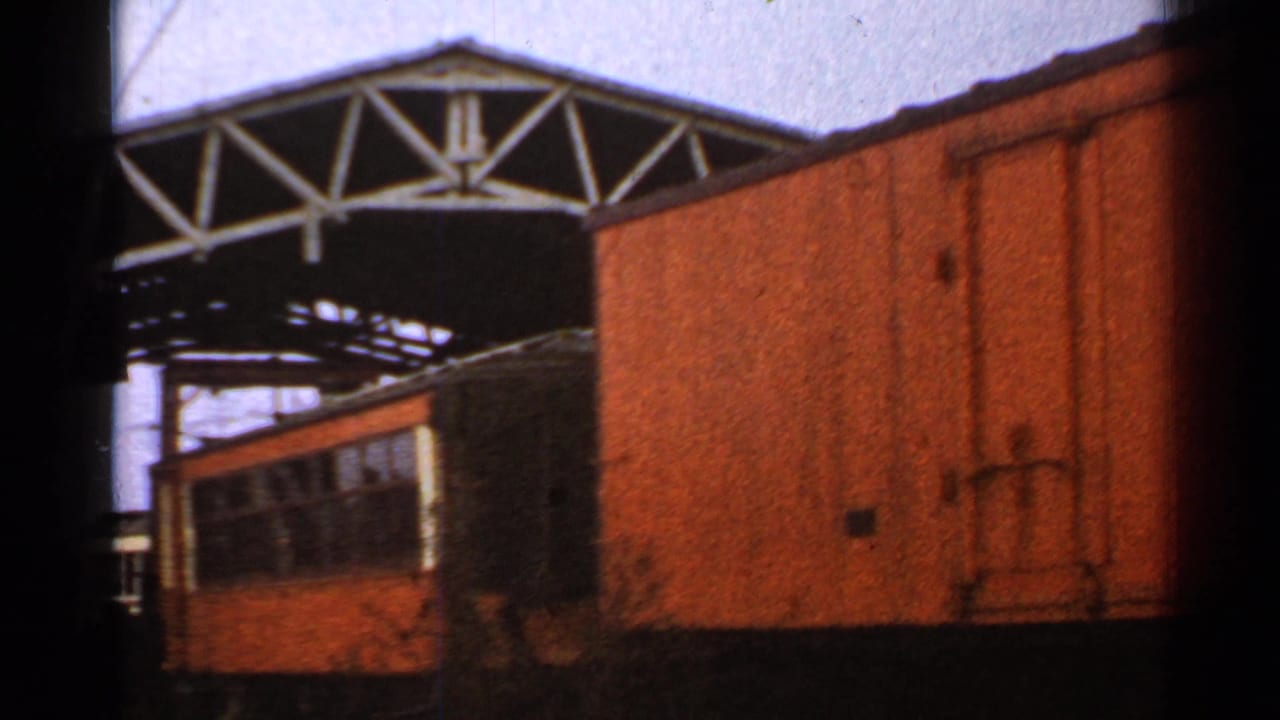 1953 Connecticut rail-yard frame with a large orange railcar in the foreground, another railcar beyond it, overhead wires, and a metal gantry.