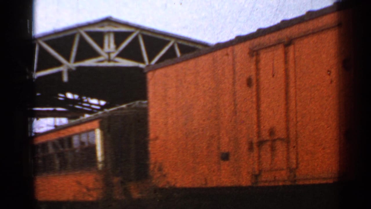1953 Connecticut rail yard view with an orange railcar, a large boxcar side, and a metal truss structure overhead.