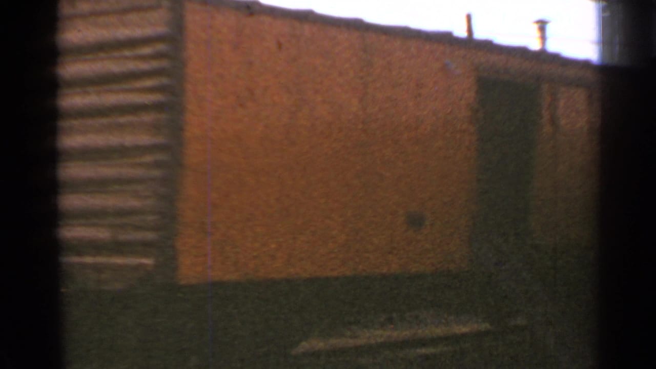 1953 Connecticut 8mm frame showing a weathered brick building and rail yard foreground near trolley equipment.