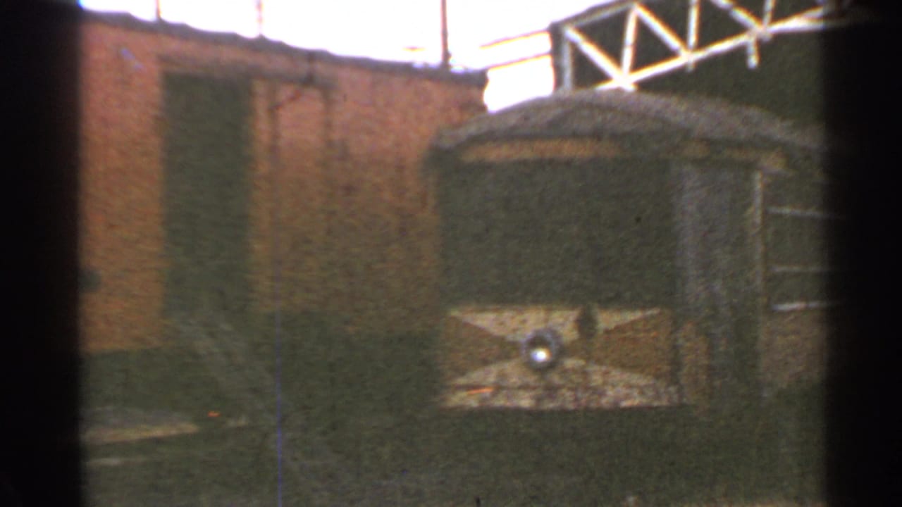 1953 Connecticut frame showing the rounded end of a trolley car with a central headlight near a brick rail yard building.