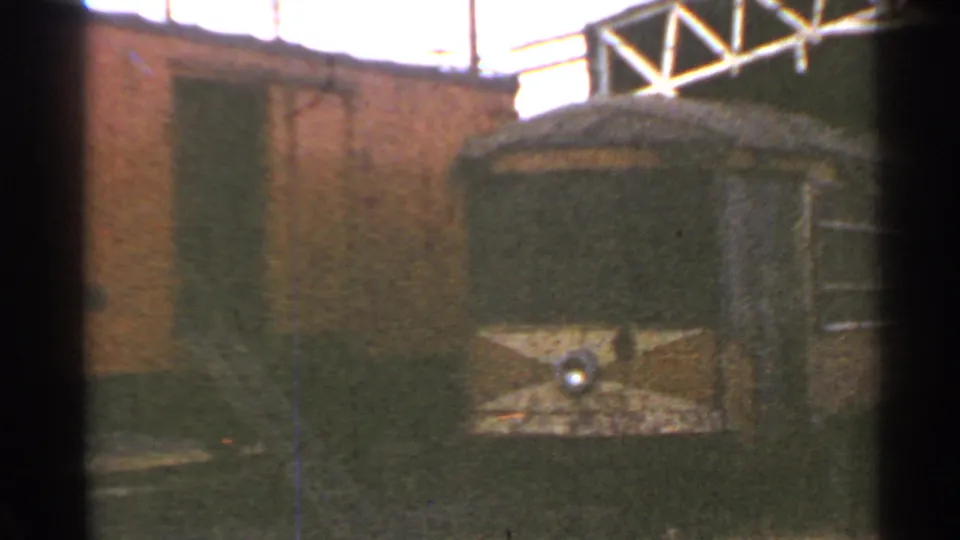 1953 Connecticut frame showing the rounded end of a trolley car with a central headlight near a brick rail yard building.