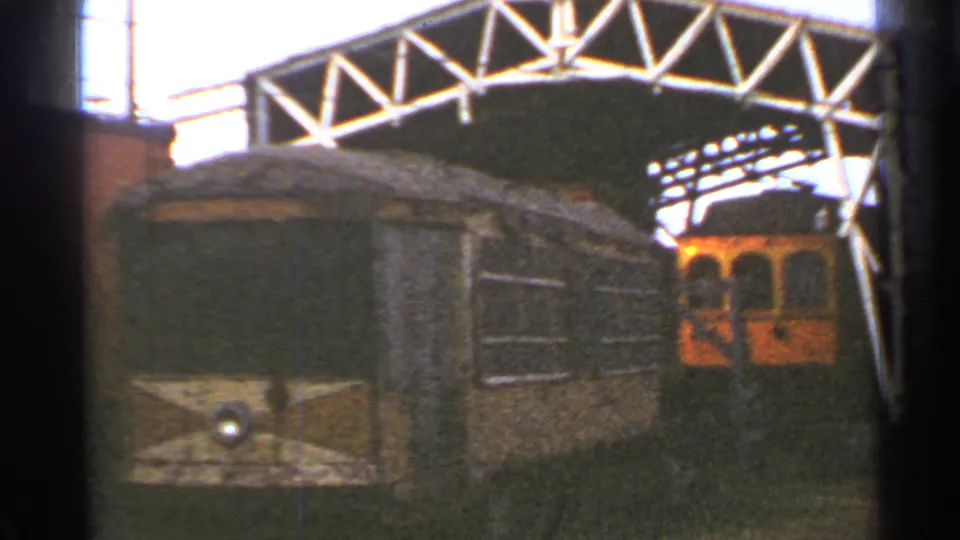 1953 Connecticut trolley yard view with a rounded railcar end, white metal truss canopy, and orange-yellow trolley behind it.
