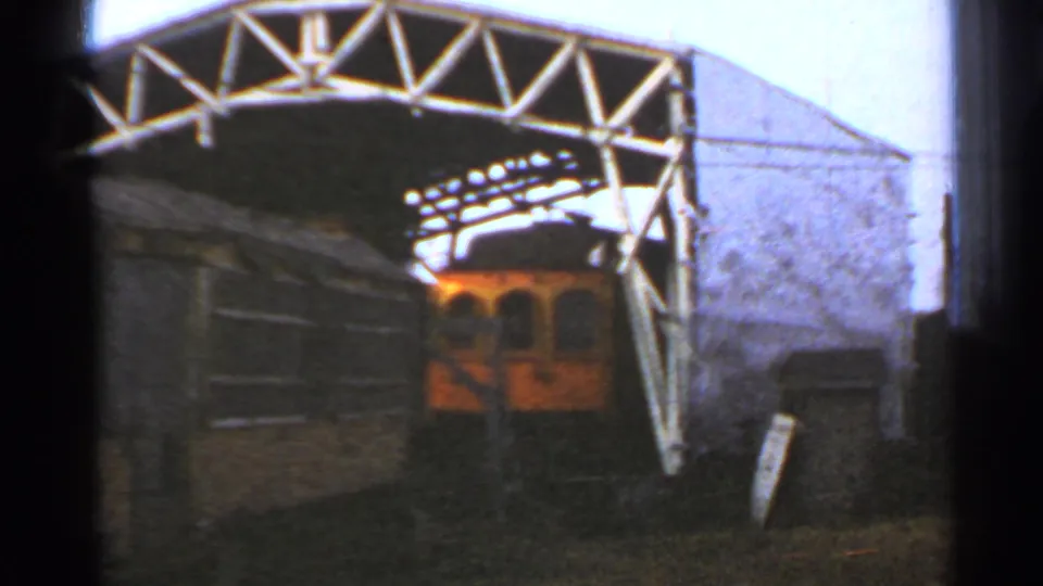 1953 Connecticut frame showing an orange-yellow trolley car parked under a white metal truss in a dark rail yard setting.