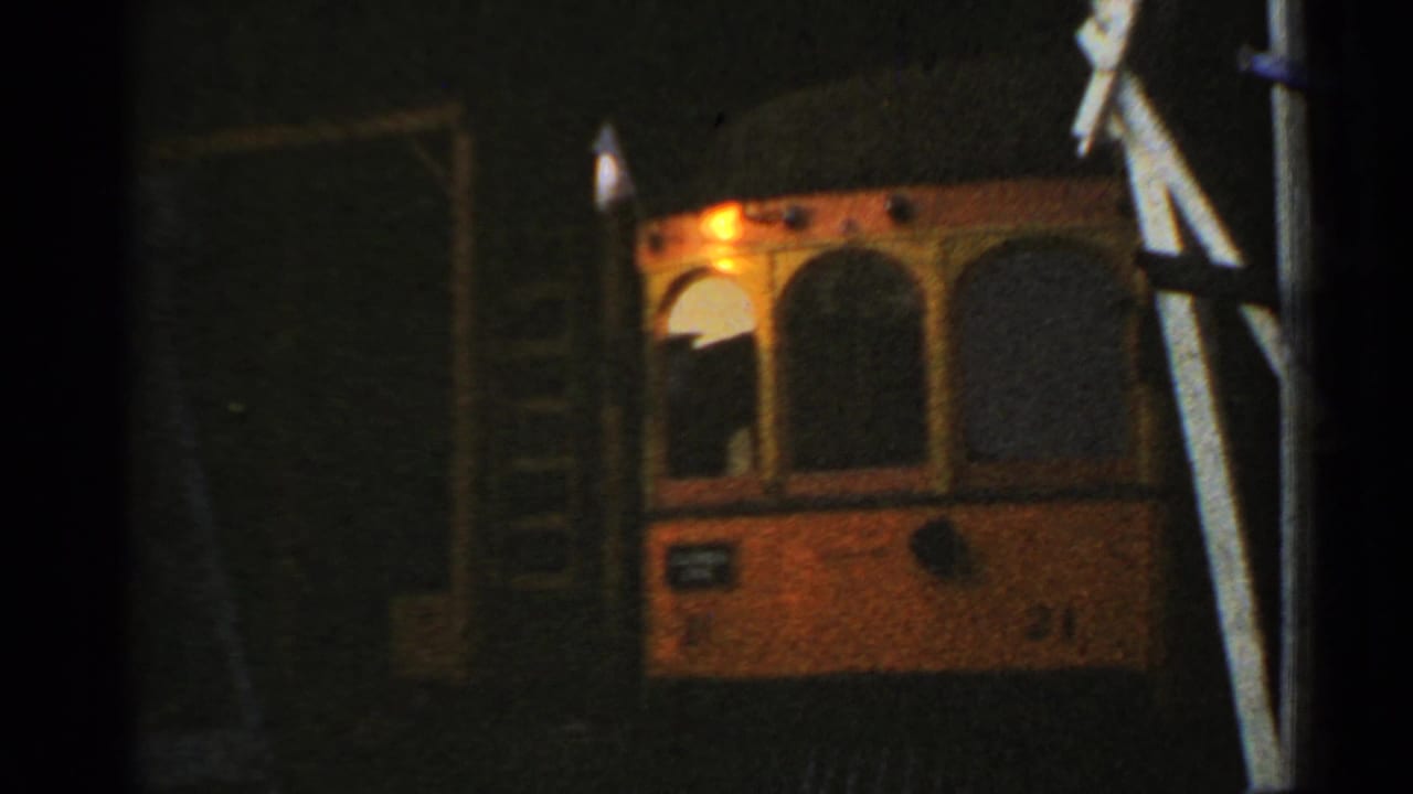 Orange and cream trolley front under a dark station canopy with one bright headlight.