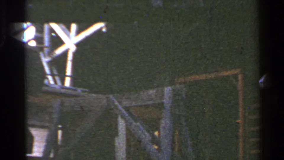 1953 Connecticut 8mm frame showing bright canopy supports, a dark station wall, and a small cropped glimpse of the trolley edge.